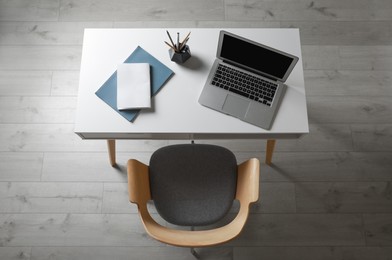 Laptop and office stationery on white table near armchair in room, above view