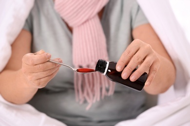 Ill mature woman taking cough syrup, closeup