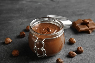 Composition with tasty chocolate cream in glass jar and hazelnuts on table