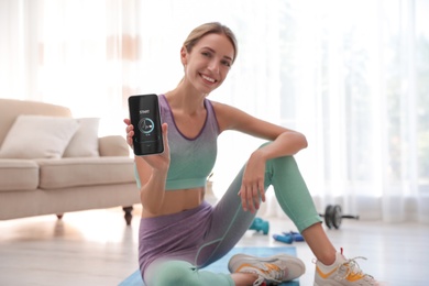 Young woman showing smartphone with fitness app at home