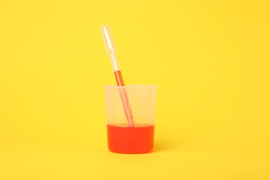 Photo of Beaker with liquid and stirring rod on yellow background. Chemical experiment toy for kids