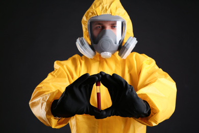 Man in chemical protective suit holding test tube of blood sample against black background. Virus research