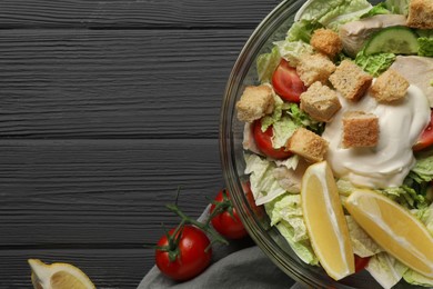 Bowl of delicious salad with Chinese cabbage, lemon, tomatoes and bread croutons on black wooden table, flat lay. Space for text