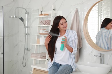 Woman applying dry shampoo onto her hair near mirror in bathroom