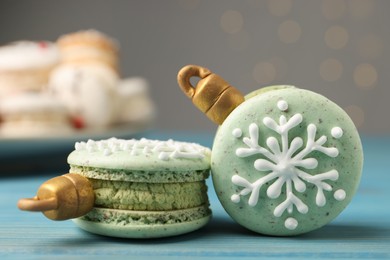 Beautifully decorated Christmas macarons on light blue wooden table against blurred festive lights, closeup