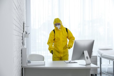 Employee in protective suit sanitizing doctor's office. Medical disinfection