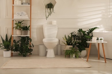 Stylish bathroom interior with white toilet bowl, tub green houseplants