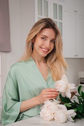 Pretty young woman in beautiful silk robe with flowers at kitchen table