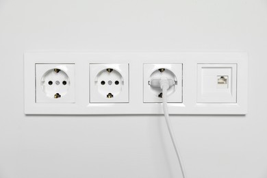 Power sockets with inserted plug on white wall. Electrical supply