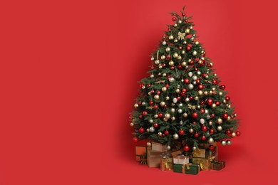 Beautifully decorated Christmas tree and many gift boxes on red background, space for text