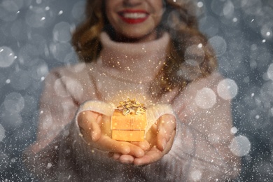 Young woman with small Christmas gift against grey background, focus on hands