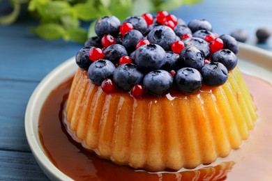 Delicious pudding with caramel and berries on blue wooden table, closeup