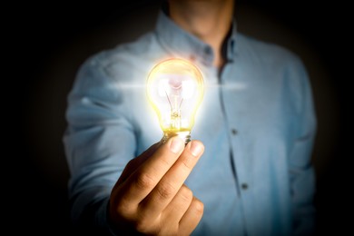 Glow up your ideas. Man holding light bulb on dark background, closeup