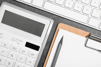 Calculator, clipboard and keyboard on dark grey table, flat lay. Tax accounting