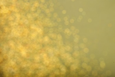 Blurred view of golden lights on pale green background. Bokeh effect