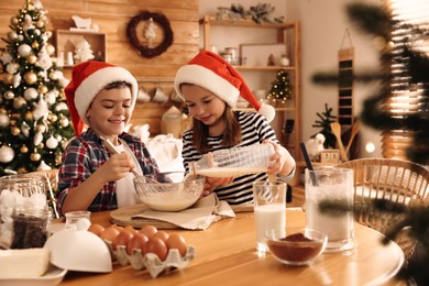 Cute little children making dough for Christmas cookies at home