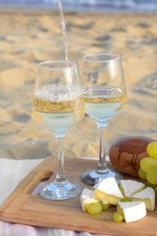 Pouring white wine into glasses on picnic blanket near sea