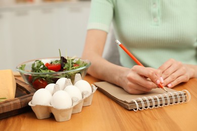 Woman writing in notebook near products at table, closeup. Keto diet