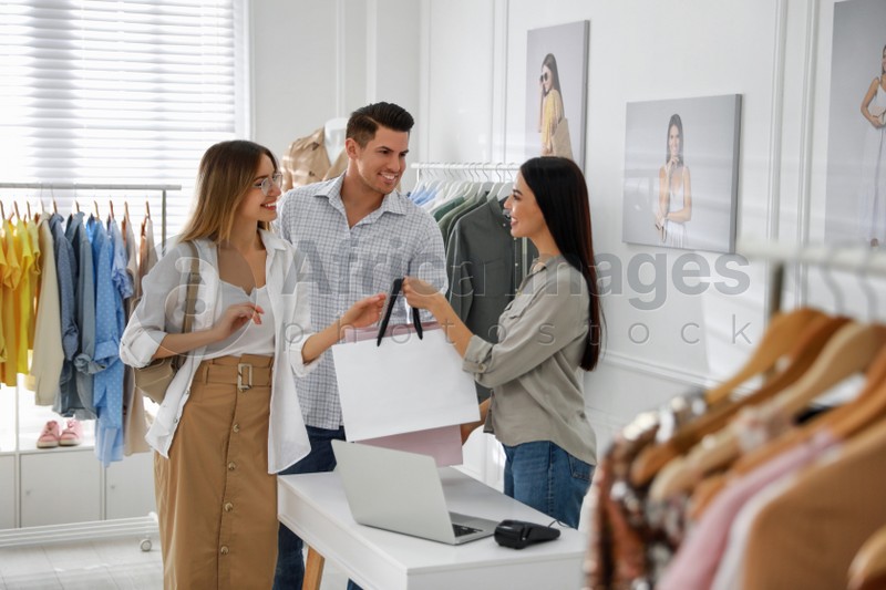 Photo of Shop assistant giving bags with clothes to couple in modern boutique