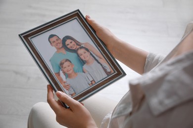 Woman holding framed family photo indoors, closeup