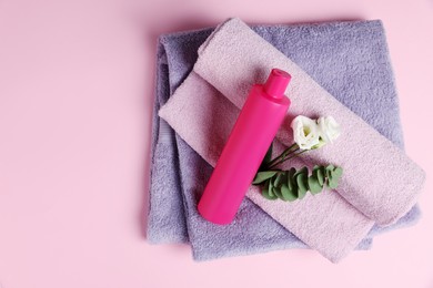 Soft folded towels with flowers, eucalyptus branch and cosmetic product on pink background, top view. Space for text