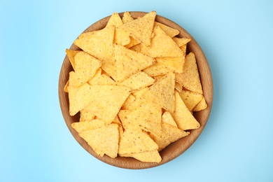 Wooden bowl of tasty Mexican nachos chips on light blue background, top view