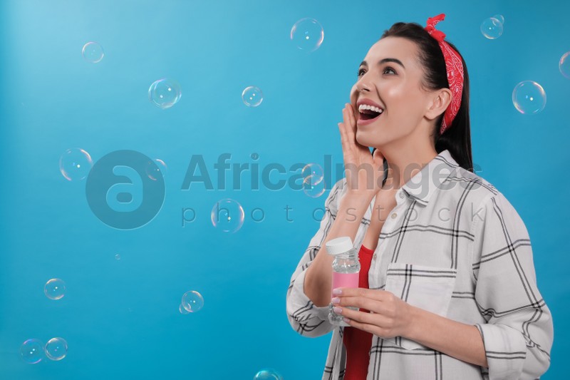 Young woman having fun with soap bubbles on light blue background, space for text