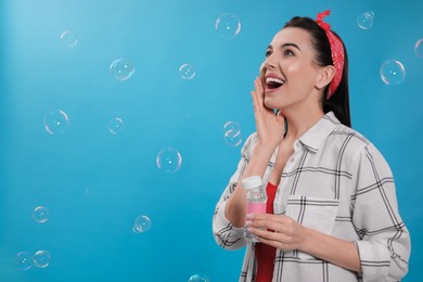 Photo of Young woman having fun with soap bubbles on light blue background, space for text