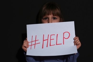 Photo of Abused little girl with hashtag HELP near black wall. Domestic violence concept