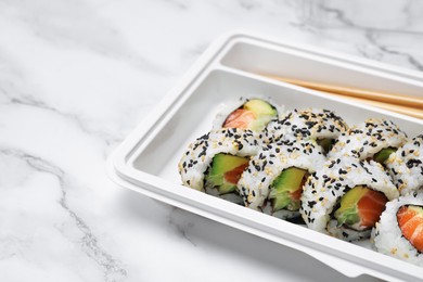 Food delivery. Delicious sushi rolls in plastic container on white marble table