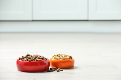 Photo of Bowls with dry dog food on white floor indoors, space for text