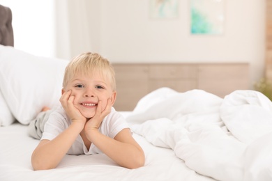 Cute little boy lying on bed at home. Space for text