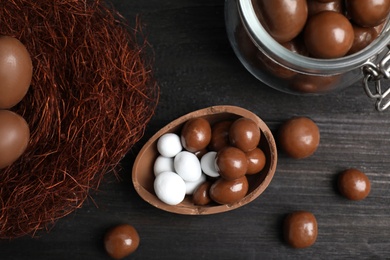 Half of tasty chocolate egg, decorative nest and candies on black wooden table, flat lay