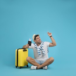 Male tourist holding passport with ticket and toy airplane near suitcase on turquoise background, space for text