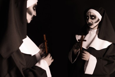 Photo of Scary devilish nun with cross near mirror on black background. Halloween party look