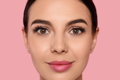 Beautiful young woman with long eyelashes on pink background, closeup