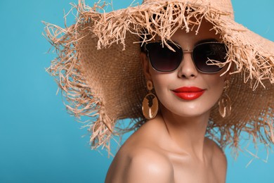 Attractive woman in fashionable sunglasses and wicker hat against light blue background. Space for text
