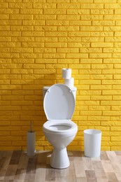 Simple bathroom interior with toilet bowl near yellow brick wall indoors. Home design