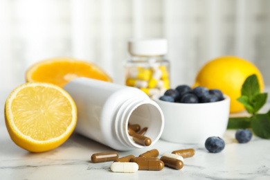 Bottle with vitamin pills, blueberries and lemon on white marble table