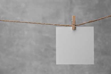 Wooden clothespin with blank notepaper on twine against grey background. Space for text