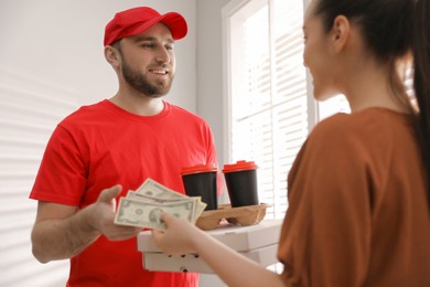 Young deliveryman receiving tips from woman indoors