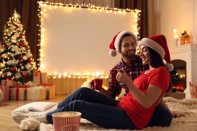 Photo of Couple watching movie on projection screen in room decorated for Christmas. Home TV equipment