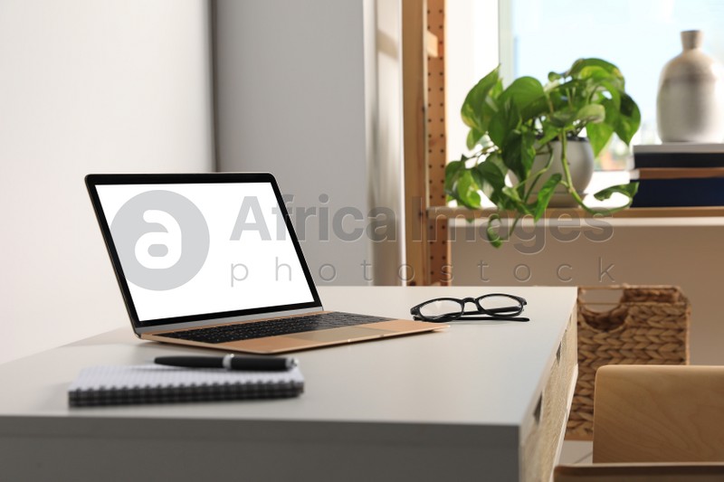 Workplace with modern laptop and glasses on white table. Mockup for design
