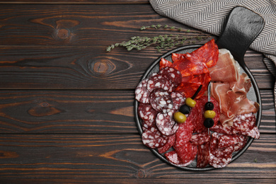 Photo of Tasty prosciutto and other delicacies served on wooden table, flat lay. Space for text