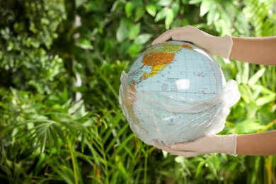 Woman holding globe in plastic bag against green leaves, closeup. Space for text. Environmental conservation