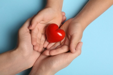 Closeup of woman and child holding heart on blue background, top view. Donation concept