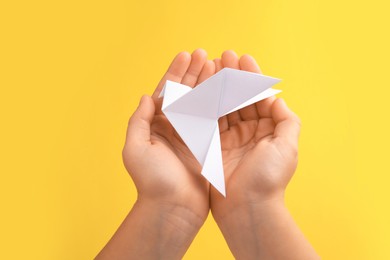 Photo of Origami art. Child holding paper bird on yellow background, closeup