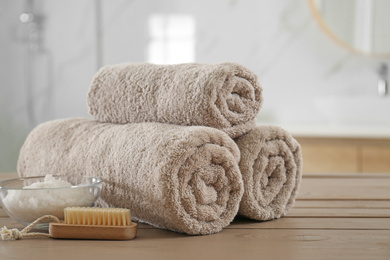 Clean rolled towels, cosmetic salt and brush on wooden table in bathroom
