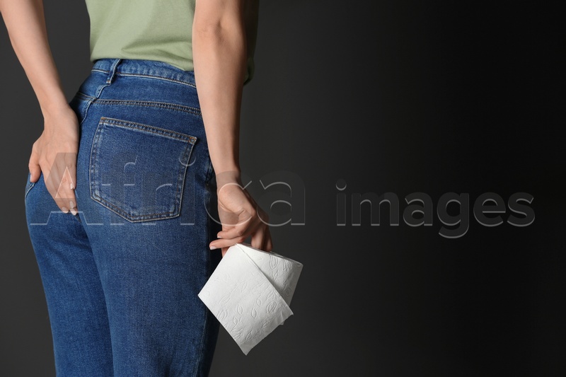 Woman with toilet paper suffering from hemorrhoid on black background, closeup. Space for text