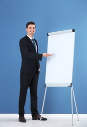 Business trainer giving presentation on flip chart board against color wall background